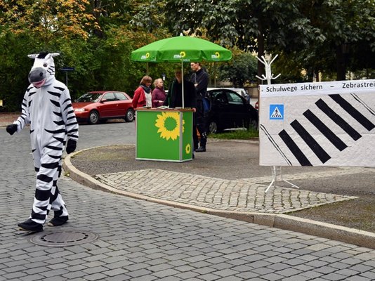 Grüne Aktion für Zebrastreifen am Stresemannplatz (Mobilitätswoche Dresden 2021) Zebra läuft über die Straße, im Hintergrund Infostand und Gespräche mit Elternvertretern 